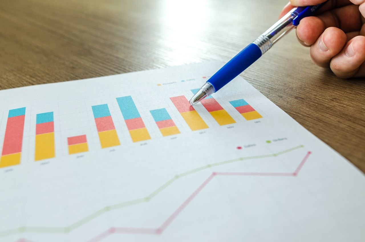 Crafting Captivating Headlines: Your awesome post title goes here Detailed close-up of a hand pointing at colorful charts with a blue pen on wooden surface.